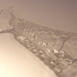 Puede incluir: Un jarr&oacute;n de vidrio transparente con un patr&oacute;n geom&eacute;trico texturizado. El jarr&oacute;n tiene una base hexagonal ensanchada y un cuerpo largo y cil&iacute;ndrico. El vidrio es transparente y est&aacute; ligeramente inclinado hacia la izquierda.