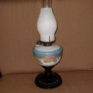 May include: A vintage oil lamp with a white glass shade and a black base. The lamp has a floral design on the base and a blue and white painted design on the globe.