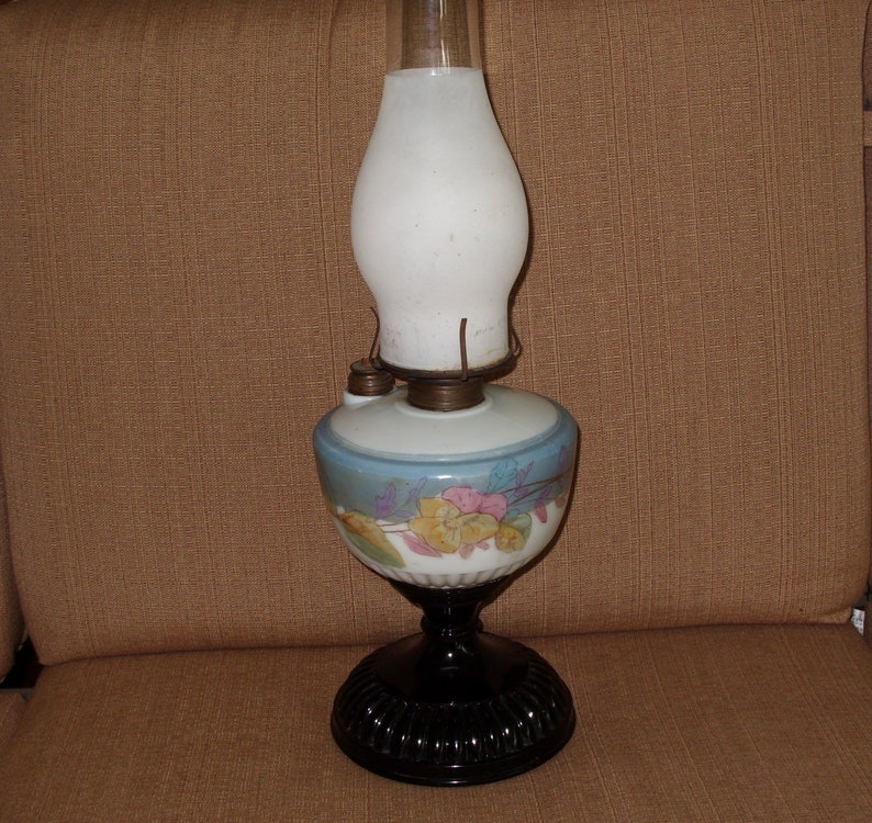May include: A vintage oil lamp with a white glass shade and a black base. The lamp has a floral design on the base and a blue and white painted design on the globe.