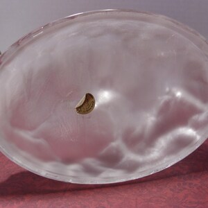 May include: A clear, oval-shaped glass bowl with a frosted appearance. The bowl has a small, circular sticker on the inside. The bowl is likely used for decorative purposes or serving food.
