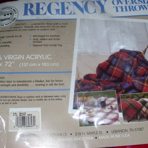 Op de afbeelding: Oversized plaid deken in rood, blauw en geel. De deken is 137 cm x 183 cm en gemaakt van 100% virgin acrylic. De verpakking bevat de tekst "REGENCY" en "TENNESSEE WOOLEN MILLS".