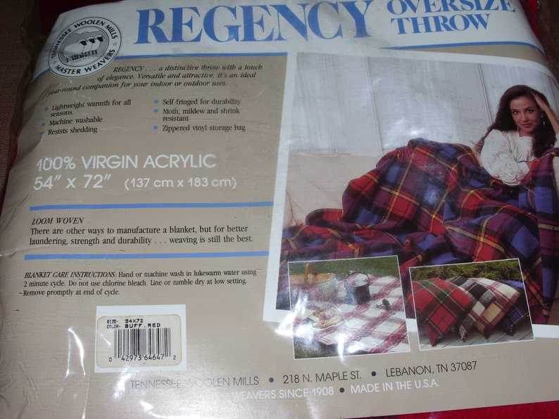 Op de afbeelding: Oversized plaid deken in rood, blauw en geel. De deken is 137 cm x 183 cm en gemaakt van 100% virgin acrylic. De verpakking bevat de tekst "REGENCY" en "TENNESSEE WOOLEN MILLS".