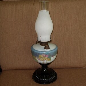 May include: A vintage oil lamp with a white frosted glass shade and a floral patterned base. The base is blue and white with a black pedestal.