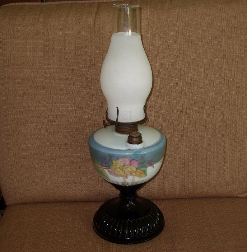 May include: A vintage oil lamp with a white frosted glass shade and a floral patterned base. The base is blue and white with a black pedestal.