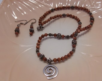 May include: A set of brown stone and silver bead jewelry with a spiral pendant. The necklace and earrings are made with brown stone beads and silver accents.