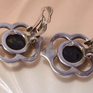 May include: A pair of silver tone clip-on earrings with a black stone set in a floral design.