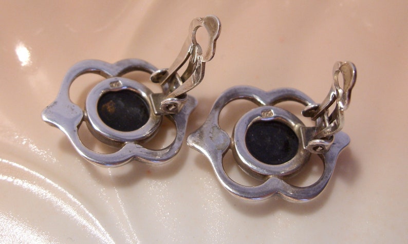 May include: A pair of silver tone clip-on earrings with a black stone set in a floral design.