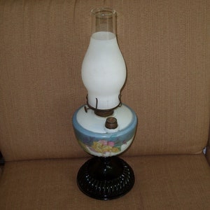 May include: A vintage oil lamp with a white frosted glass shade and a blue and white floral patterned base. The base has a black metal bottom.