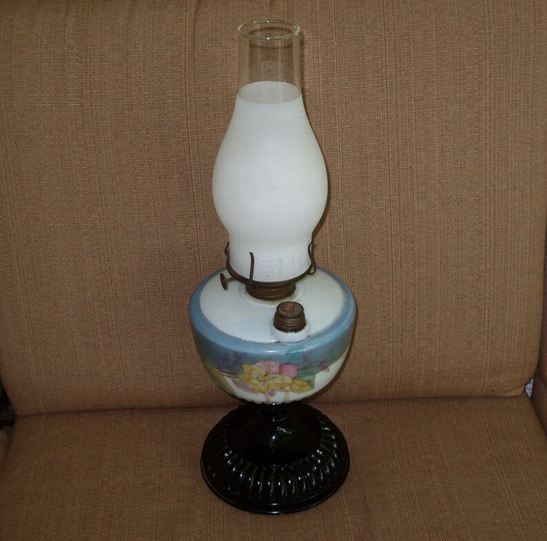 May include: A vintage oil lamp with a white frosted glass shade and a blue and white floral patterned base. The base has a black metal bottom.