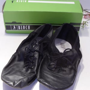 Puede incluir: Zapatos de baile de cuero negro con cordones, frente a una caja verde con el logo de Bloch. Los zapatos tienen un dise&ntilde;o suave y flexible, adecuado para varios estilos de baile. La caja est&aacute; en el fondo.