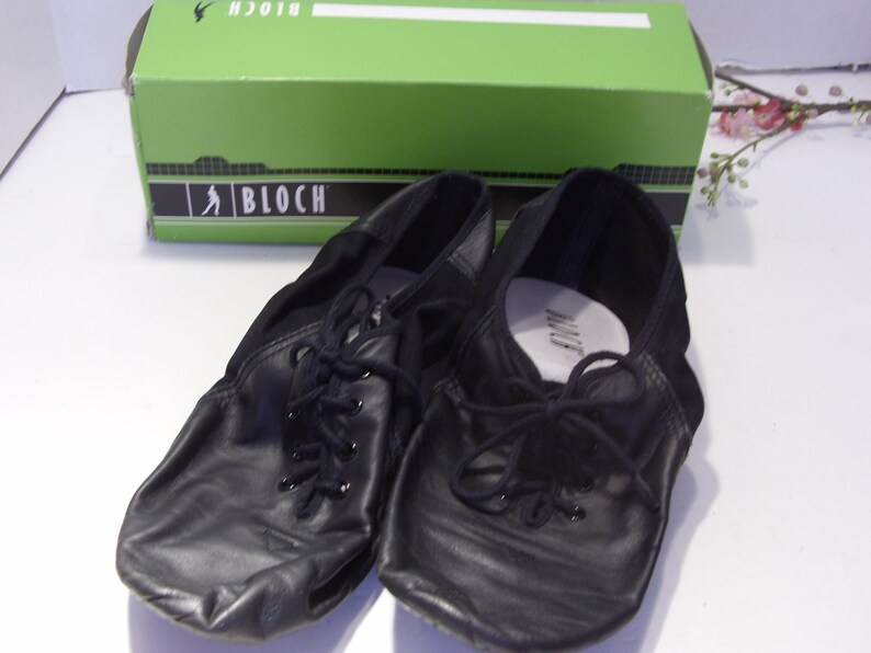 Puede incluir: Zapatos de baile de cuero negro con cordones, frente a una caja verde con el logo de Bloch. Los zapatos tienen un dise&ntilde;o suave y flexible, adecuado para varios estilos de baile. La caja est&aacute; en el fondo.
