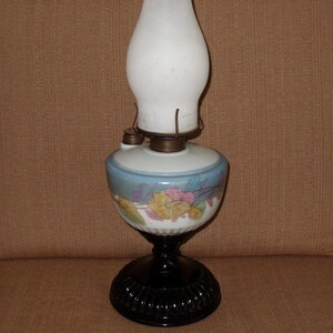 May include: A vintage oil lamp with a white glass shade and a blue and white floral design on the base. The lamp has a black metal base.