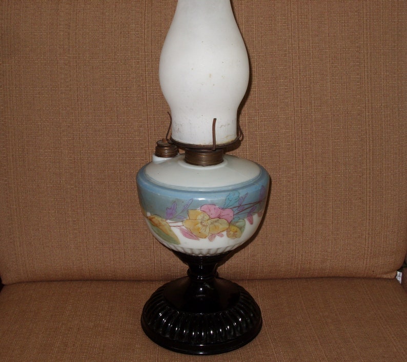May include: A vintage oil lamp with a white glass shade and a blue and white floral design on the base. The lamp has a black metal base.