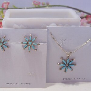 May include: A set of sterling silver earrings and a necklace with turquoise flower pendants. The earrings and pendant are both in the shape of a flower with a turquoise center and silver petals. The cards say "Sterling Silver".