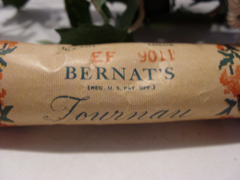 May include: Close-up of a vintage Bernat's Tournan yarn label. The label is tan with the name "BERNAT'S" in blue, and "Tournan" in a script font. The label also has the text "(REG. U.S. PAT. OFF.)" and the number "9011".