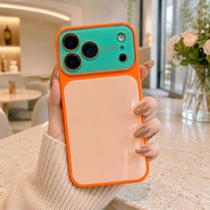 Op de afbeelding: Een rechthoekig smartphonehoesje met een feloranje frame en een gladde, licht perzikkleurige achterkant. Het bovenste gedeelte bevat een levendige blauwgroene cameramodule met drie ronde uitsparingen en de tekst AUTO FOCUS.
