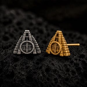 May include: Two stud earrings shaped like stepped pyramids, one in a silver-tone finish and one in a gold-tone finish. Each pyramid features a central circular door design with vertical bars and a post extending from the back of the gold earring.