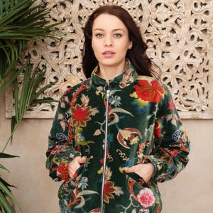 Pode incluir: Um blusão bomber de veludo verde-escuro com um padrão floral vibrante em tons de vermelho, laranja, amarelo e azul. O casaco possui um fecho de correr prateado à frente, gola alta, mangas compridas com punhos elásticos e dois bolsos laterais.