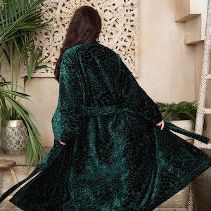 May include: A long, dark emerald green velvet robe featuring a textured, repeating honeycomb or hexagonal pattern throughout the fabric. The garment includes long sleeves, a matching tie belt at the waist, and a flared, open-front design.
