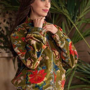 May include: A long-sleeve olive green velvet bomber jacket featuring a vibrant floral pattern in shades of red, blue, and yellow. The jacket includes a silver-toned front zipper, a high collar, and elasticized cuffs and hem for a gathered fit.