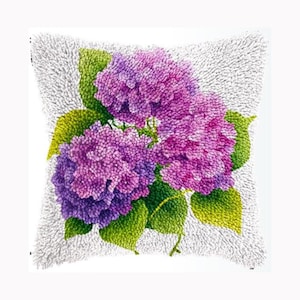 Könnte beinhalten: Ein quadratisches Zierkissen mit einer texturierten, getufteten Oberfläche und einem zentralen Motiv aus leuchtend violetten und rosafarbenen Hortensienblüten, umgeben von hellgrünen Blättern auf weißem Grund, gefertigt in Punch-Needle-Technik.