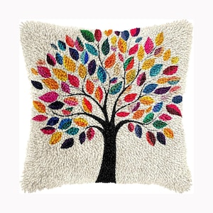Könnte beinhalten: Ein quadratisches Kissen mit einer strukturierten, cremeweißen Oberfläche aus Schlingenflor. In der Mitte befindet sich ein Punch-Needle-Design eines Baumes mit schwarzem Stamm und Ästen, verziert mit zahlreichen kleinen, bunten Blättern in Rot, Gelb, Blau, Grün und Violett.
