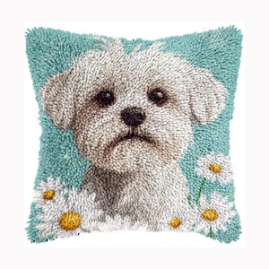 Peut inclure: Un coussin carré avec un motif en punch needle texturé représentant un chien blanc aux yeux sombres et au nez noir. Le fond est bleu clair uni et les coins inférieurs sont décorés de marguerites blanches aux cœurs jaunes.
