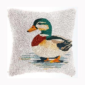May include: A square throw pillow featuring a textured, tufted design of a mallard duck. The duck has a green head, a yellow beak, a reddish-brown chest, and white and dark feathers. The background of the pillow is a light, off-white color.