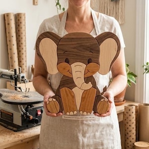 Op de afbeelding: Een decoratief houten olifantfiguur gemaakt van verschillende houttinten, met grote oren, een gekrulde slurf en afgeronde voeten. Het ontwerp gebruikt contrasterende lichte en donkere houtnerven om de gelaatstrekken en lichaamsdelen te definiëren.