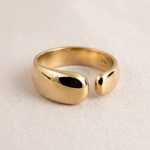 Puede incluir: Un anillo abierto de oro pulido con un diseño de banda lisa, redondeada y gruesa. El interior de la banda presenta un pequeño y claro grabado que dice 14K, indicando la pureza del metal de esta pieza de joyería de oro macizo.