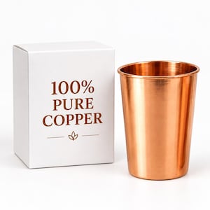 Könnte beinhalten: Ein glänzender, metallischer Kupferbecher mit glatter Oberfläche, der neben einer weißen rechteckigen Schachtel steht. Die Schachtel trägt den braun aufgedruckten Text 100% PURE COPPER und ein kleines Blattsymbol unter dem Text.