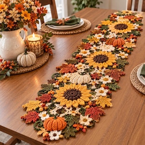 Può includere: Un lungo runner da tavola all'uncinetto caratterizzato da un motivo ripetuto di girasoli gialli con centri marrone scuro, zucche arancioni e bianche, foglie d'acero rosse e arancioni e piccoli fiori bianchi, collegati da un fogliame verde all'uncinetto.