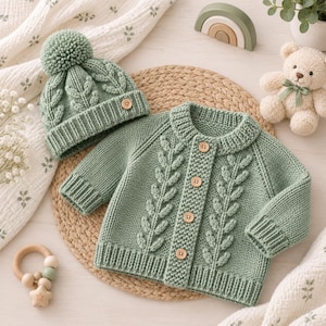 Può includere: Un set composto da cardigan e berretto in maglia color verde salvia per neonati. Il cardigan presenta un'abbottonatura frontale con bottoni in legno e un motivo a trecce a forma di foglia. Il berretto ha un grande pon-pon e un cuoricino in legno.
