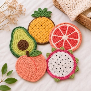 May include: A set of five fruit-shaped crochet coasters including an avocado, a pineapple, a grapefruit slice, a peach, and a dragon fruit slice. Each coaster features vibrant colors like yellow, green, pink, orange, and white with detailed stitching.