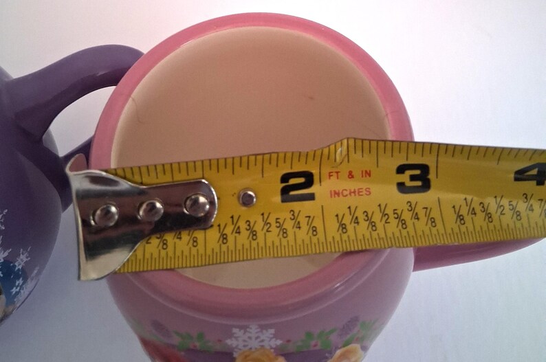 Puede incluir: Una taza de cer&aacute;mica rosa y blanca con una cinta m&eacute;trica amarilla que muestra un di&aacute;metro de aproximadamente 7,6 cm. La taza tiene un borde rosa y un dise&ntilde;o decorativo en la base.