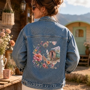 Könnte beinhalten: Eine blaue Jeansjacke mit einer großen, farbenfrohen Grafik auf der Rückseite. Das Design zeigt einen Wagen im Vintage-Stil, umgeben von lebendigen, mehrfarbigen Blumenmustern, darunter rosa, orange und violette Blüten auf hellem Grund.