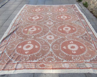 May include: A large rectangular textile featuring a repeating pattern of circular medallions in muted terracotta and off-white. The fabric displays intricate floral and vine-like embroidery motifs throughout the surface, finished with a wide decorative border.