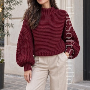 May include: A deep burgundy knit sweater featuring a mock neck, long voluminous sleeves with ribbed cuffs, and a ribbed hem. The sweater has a thick, textured horizontal stitch pattern throughout. The text TheSoftStudio is visible on the right side.