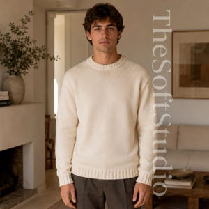 May include: A cream-coloured long-sleeve crewneck jumper with a ribbed knit collar, cuffs, and hem. The jumper features a solid, neutral tone and a classic pullover design. The text TheSoftStudio is visible on the right side of the image.