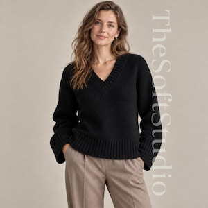 Könnte beinhalten: Ein schwarzer Langarmpullover mit tiefem V-Ausschnitt, gerippten Bündchen an Ärmeln, Saum und Ausschnitt sowie einer groben Strickstruktur. Der Text TheSoftStudio ist auf der rechten Seite des Bildes vertikal ausgerichtet zu sehen.