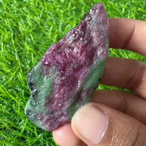 Op de afbeelding: Een ruw, ongepolijst mineraal exemplaar met een levendig magenta-rood centrum omringd door een getextureerde, lichtgroene buitenlaag. De steen heeft een onregelmatige, langwerpige vorm met een kristallijn oppervlak dat licht reflecteert.