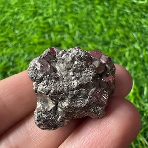 May include: A raw, metallic pyrite mineral specimen featuring a cluster of cubic, brass-colored crystals with a reflective, multifaceted surface. The stone displays a natural, irregular shape with sharp, geometric edges and a dense, textured appearance.