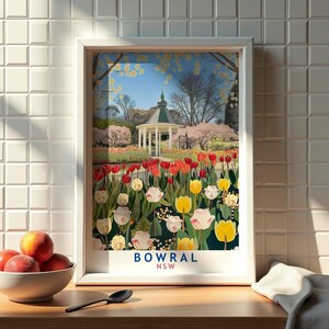 May include: A framed art print featuring a white gazebo in a garden filled with red, yellow, and white tulips under a blue sky. The text "BOWRAL NSW" is printed in blue and red at the bottom of the print, which is housed in a white frame.