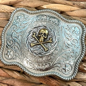 May include: Silver belt buckle with an ornate design featuring a gold skull and crossbones in the center.