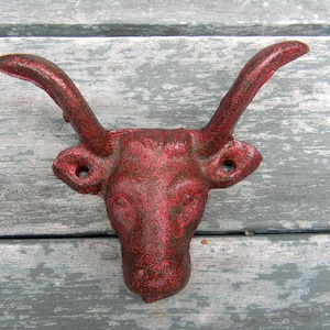 Peut inclure: Crochet mural en fonte rouge en forme de tête de taureau. Le crochet est en forme de tête de taureau avec des cornes et une surface texturée.