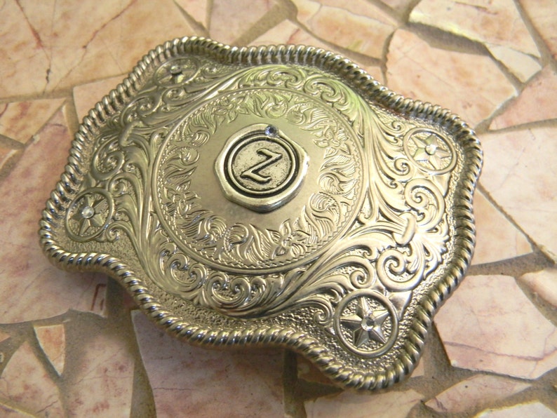 Puede incluir: Hebilla de cintur&oacute;n de plata con un dise&ntilde;o ornamentado y una letra "Z" en relieve en el centro.