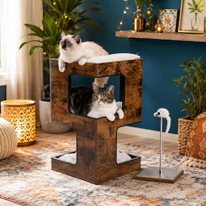 May include: A multi-level cat tower made of dark brown wood with a distressed finish, featuring a square cubby hole and soft white cushions. A separate metal stand with a small white plush toy mouse on a spring sits next to the cat furniture.