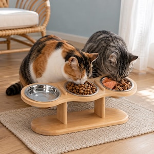 May include: A light-colored wooden elevated pet feeder stand featuring three circular cutouts holding stainless steel bowls. One bowl is empty, one contains brown dry kibble, and one contains wet food. Two cats are eating from the bowls.