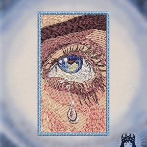 Puede incluir: Un parche rectangular bordado que muestra un ojo detallado con iris azul y una lágrima cayendo del párpado inferior. El tono de piel es bronceado claro con cejas marrones. El texto DAVISJP aparece en la esquina superior izquierda.