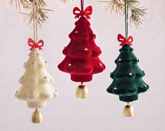 May include: Three hanging Christmas tree ornaments in white, red, and dark green velvet fabric. Each tree features small gold studs, a red fabric bow at the top, and a small gold-colored metal bell attached to the bottom base.